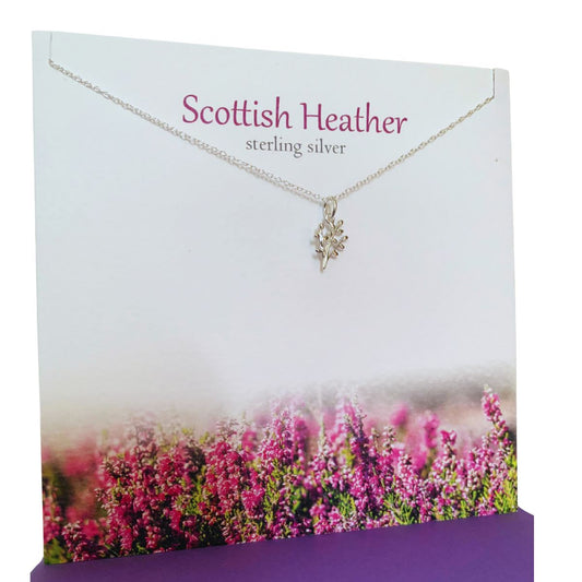 A silver necklace with a Scottish Heather pendant. It hangs on a greeting card saying 'Scottish Heather; Sterling Silver'. The card also has a photograph of purple heather along the bottom border.