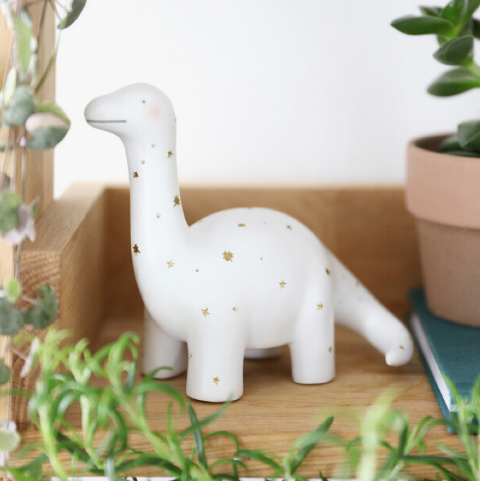 White dinosaur nightlight with gold stars surrounded by green foliage