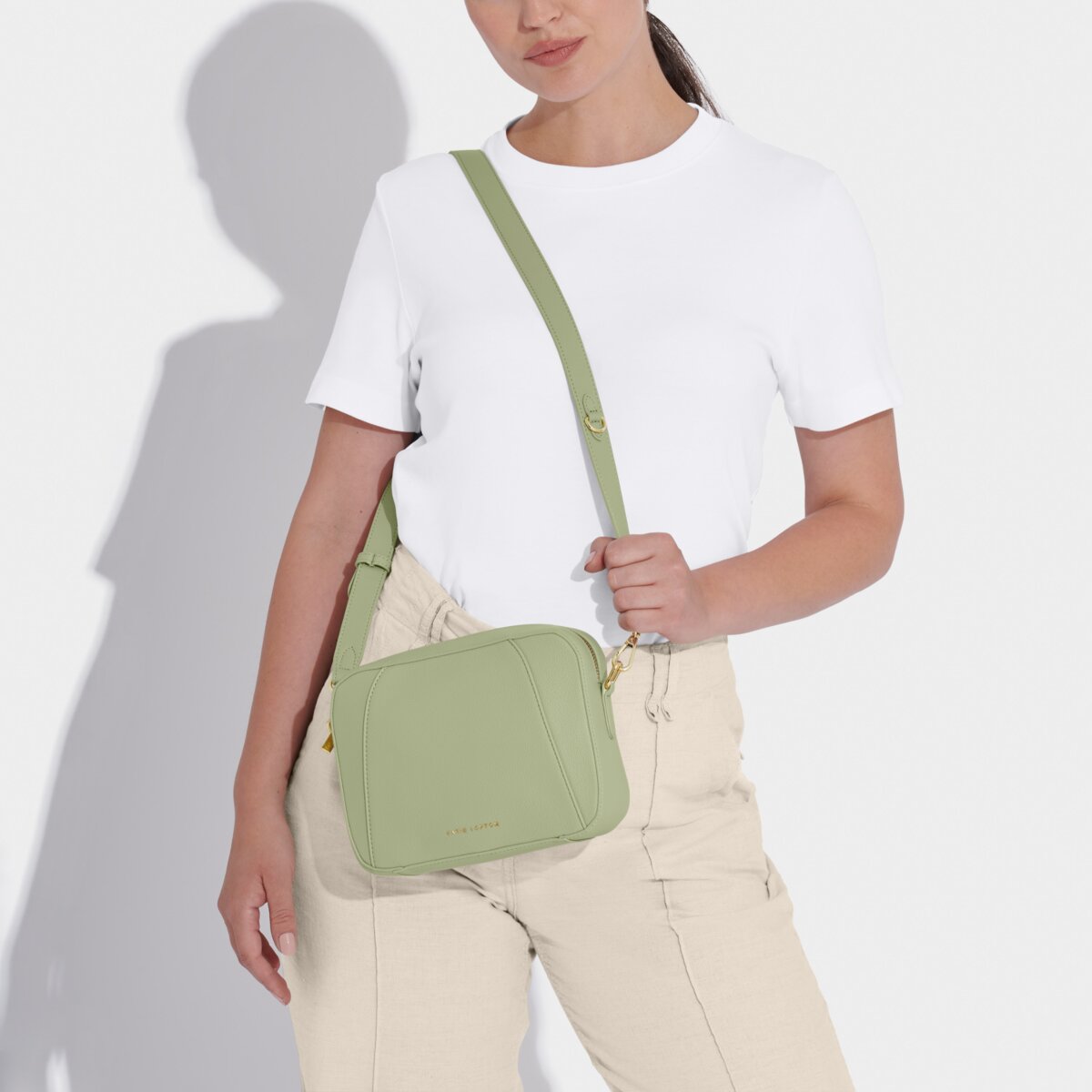 Model in a white t-shirt and cream trousers with the Crossbody handbag in soft sage greeen