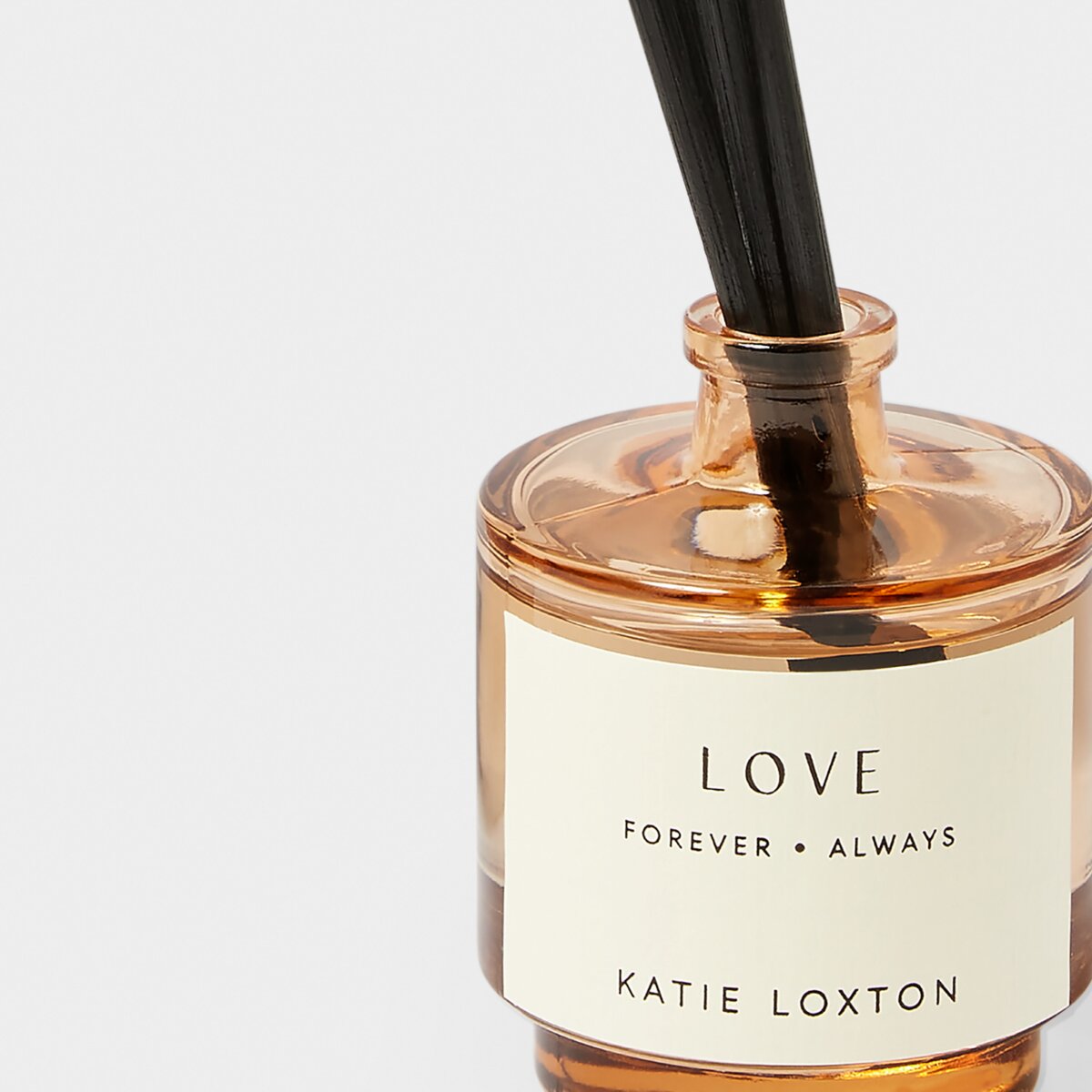 Close up of reed diffuser in an amber glass bottle with 'love' and black diffuser reeds