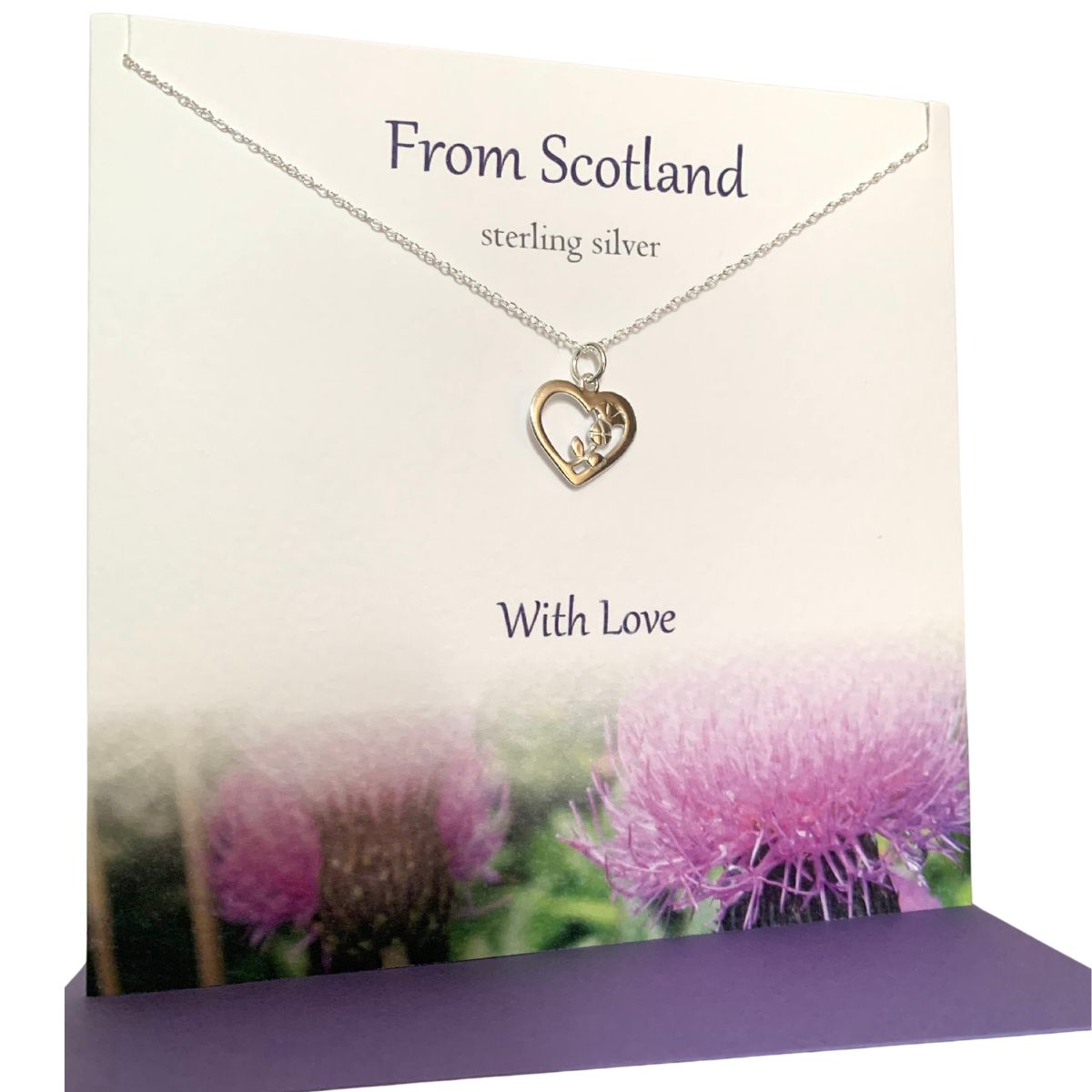 Heart shaped silver pendant necklace entwined with a thistle on a greeting card with purple thistles along the bottom border. The card says From Scotland With Love