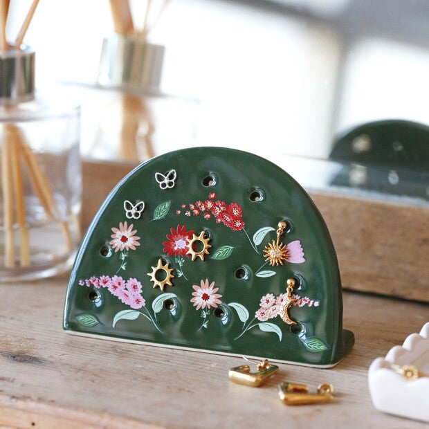 Green ceramic earring holder with floral design and gold stud earrings in the stand
