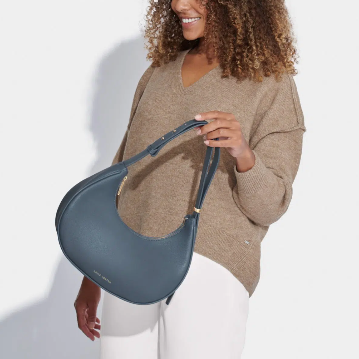 model in brown jumper and white jeans holding navy blue scoop shaped handbag