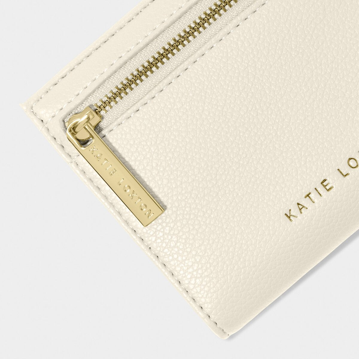 close up of purse, highlighting the katie Loxton gold zipper and gold foil Katie Loxton detaiil along bottom edge of the purse.
