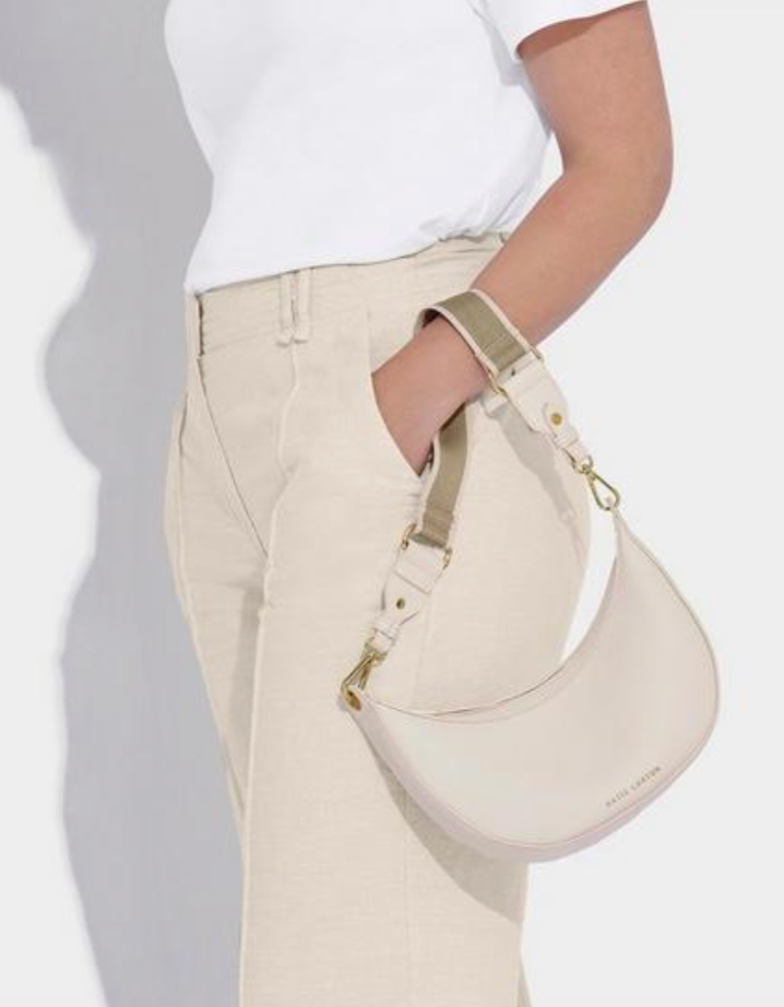 model wearing a white t-shirt and cream trousers. She has her left hand in her trouser pocket and has the off-white scoop shaped handbag around her wrist.