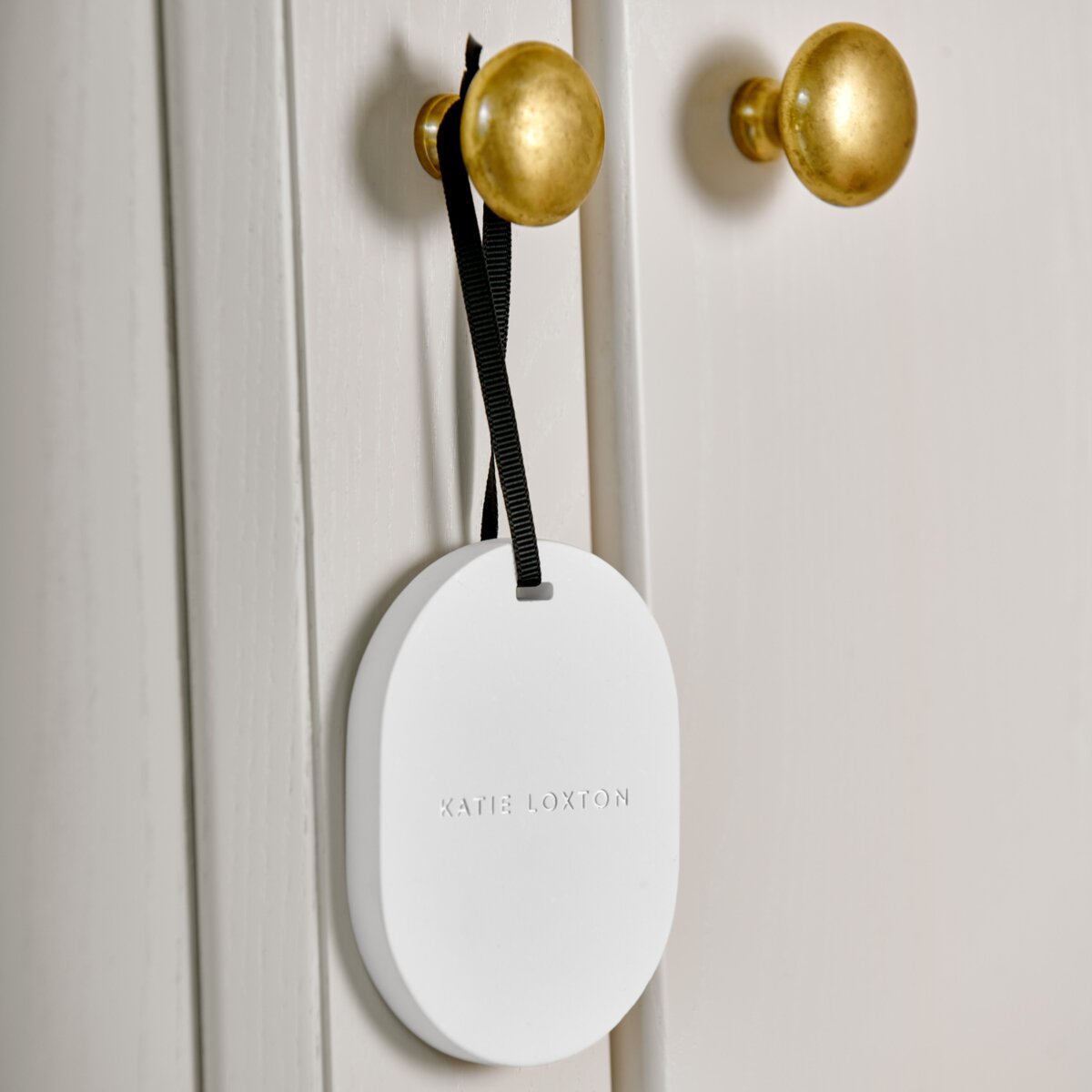 Pebble shaped white cermaic diffuser hanger hanging by its ribbon from a gold door knob.