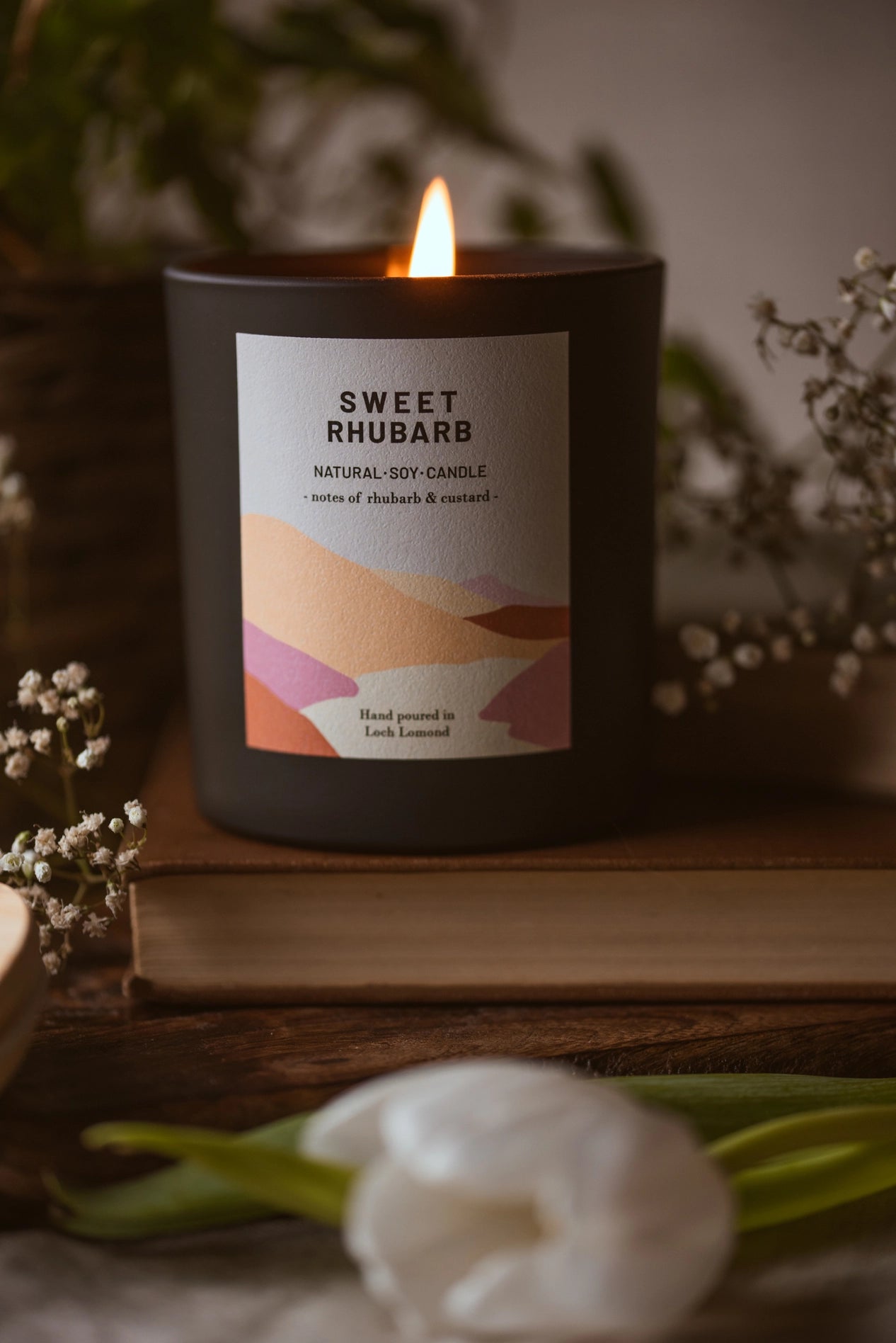 Burning Sweet Rhubarb scented candle surrounded by white flowers
