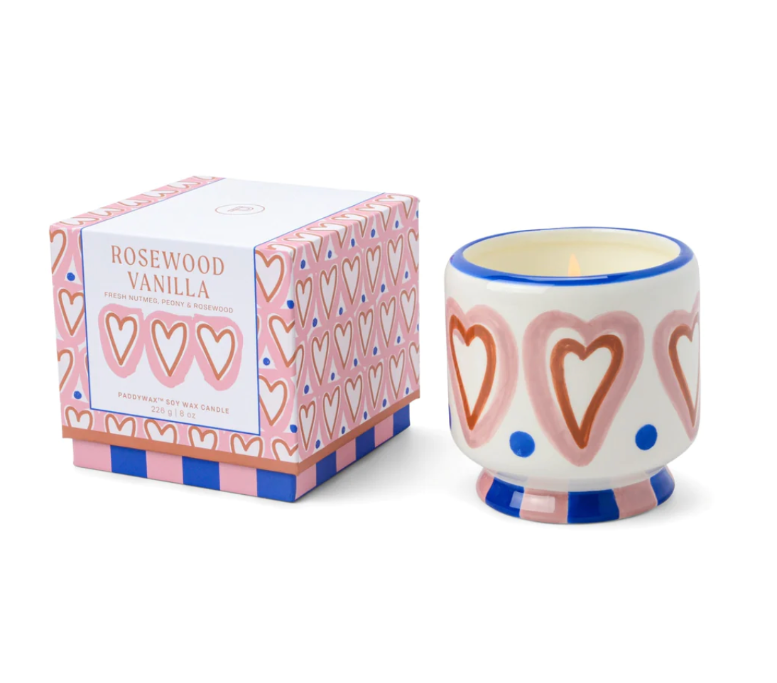 scented candle in a cermaic holder decoared with red and pink hearts with blue accents sitting beside its matching box.