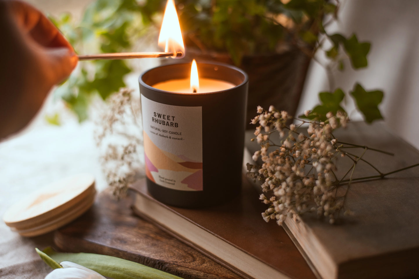 Sweet Rhubarb scented candle being lit. The candle sits on some old books