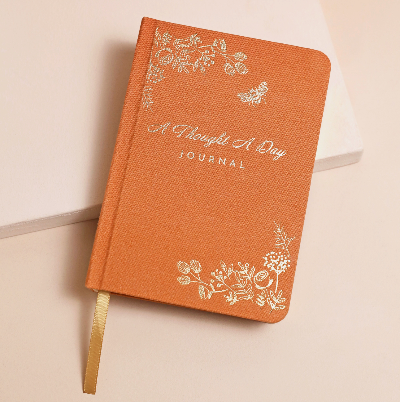 orange journal with gold floral detail and A Thought A Day Journal writing on the cover