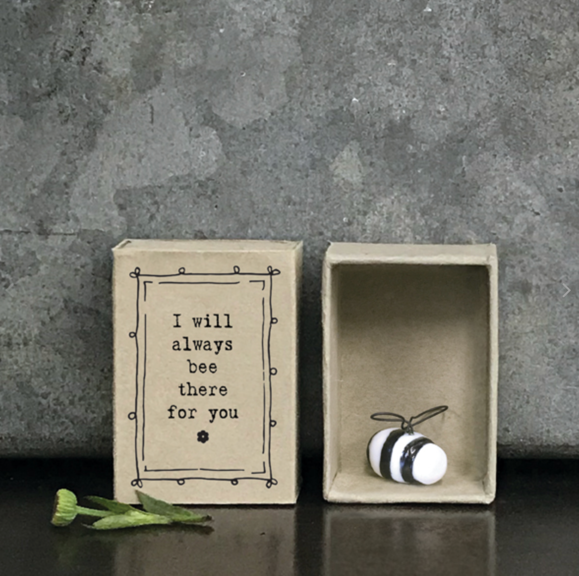 Small black and white porcelain bumble bee sitting in a small Kraft box that says 'I will always bee there fore you'. Small green flower sits to the side.